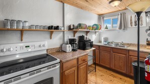 A kitchen with wooden cabinets, a stove, a microwave, and various kitchen items on shelves. - Experience comfort at The Bucking Moose (#02) The Loft, just 1 minute from Yellowstone! (West Yellowstone)