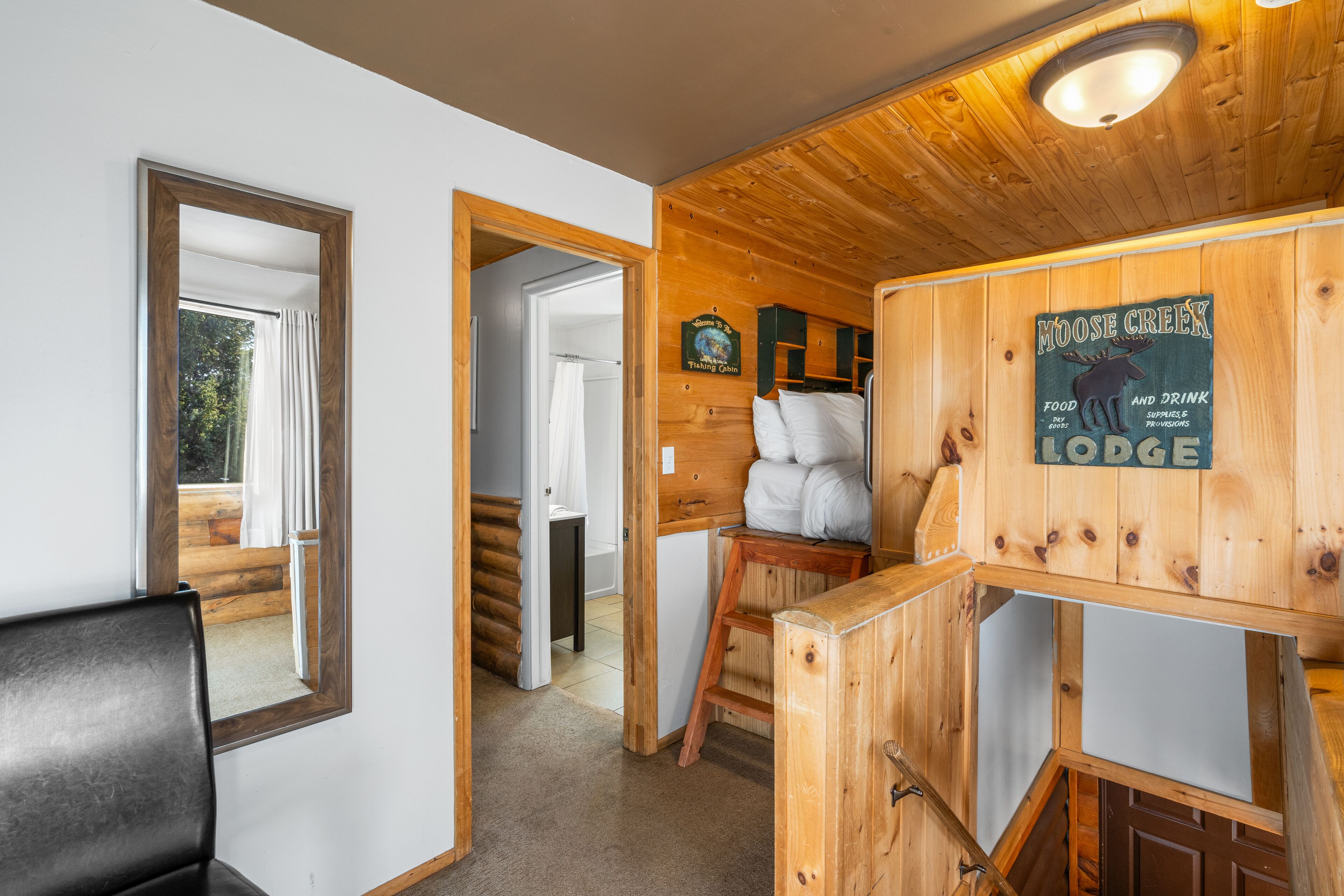 Interior de una cabaña de madera con una cama, una escalera de madera y un letrero que dice Moose Creek Lodge.