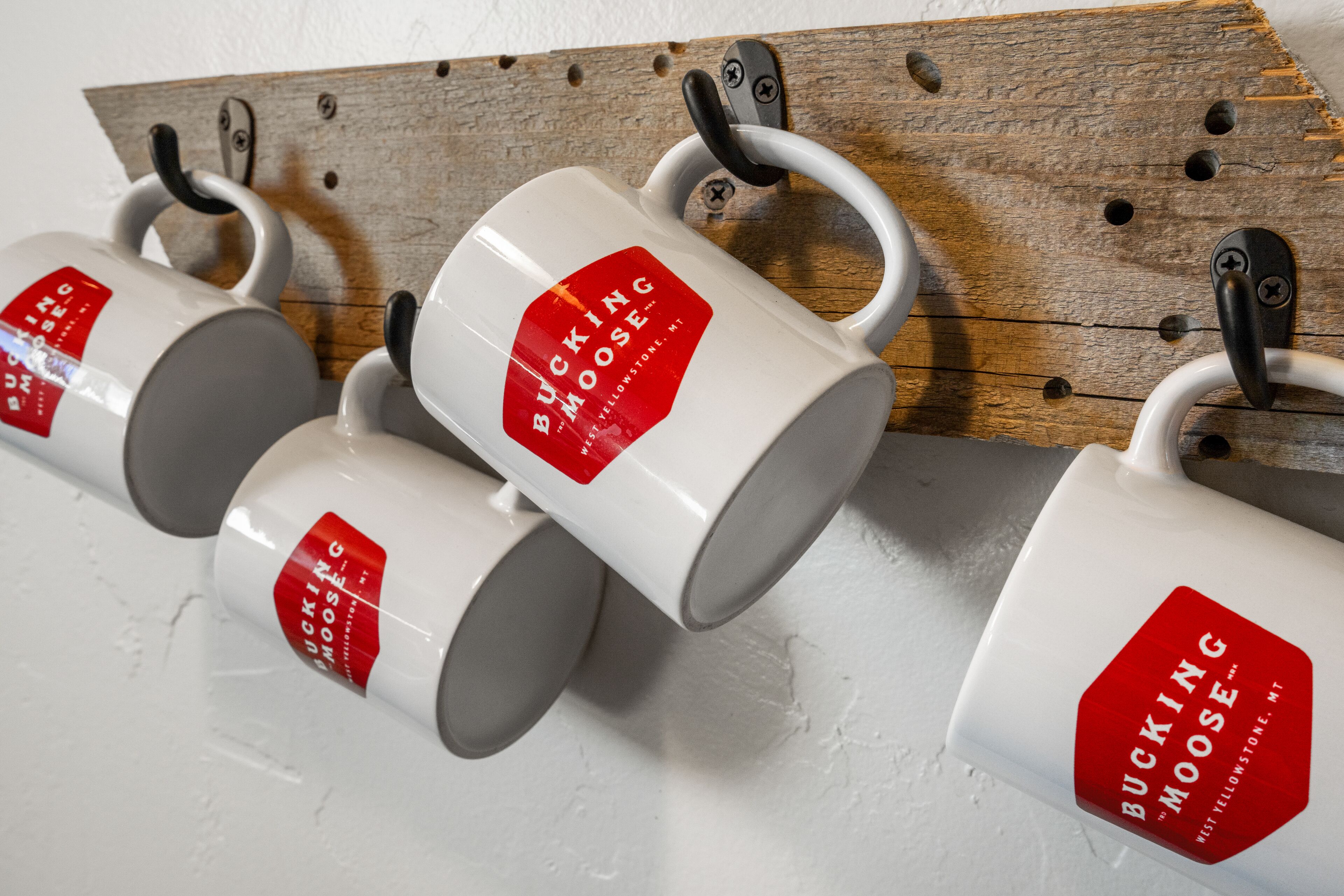 Tazas con etiqueta roja colgadas en un estante de madera.