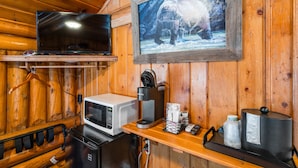 Interior de una cabaña de madera con televisor, cafetera, microondas y un cuadro con un oso.