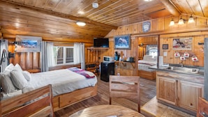 Una cabaña de madera con una cama, una mesa de comedor, una zona de cocina y un televisor.