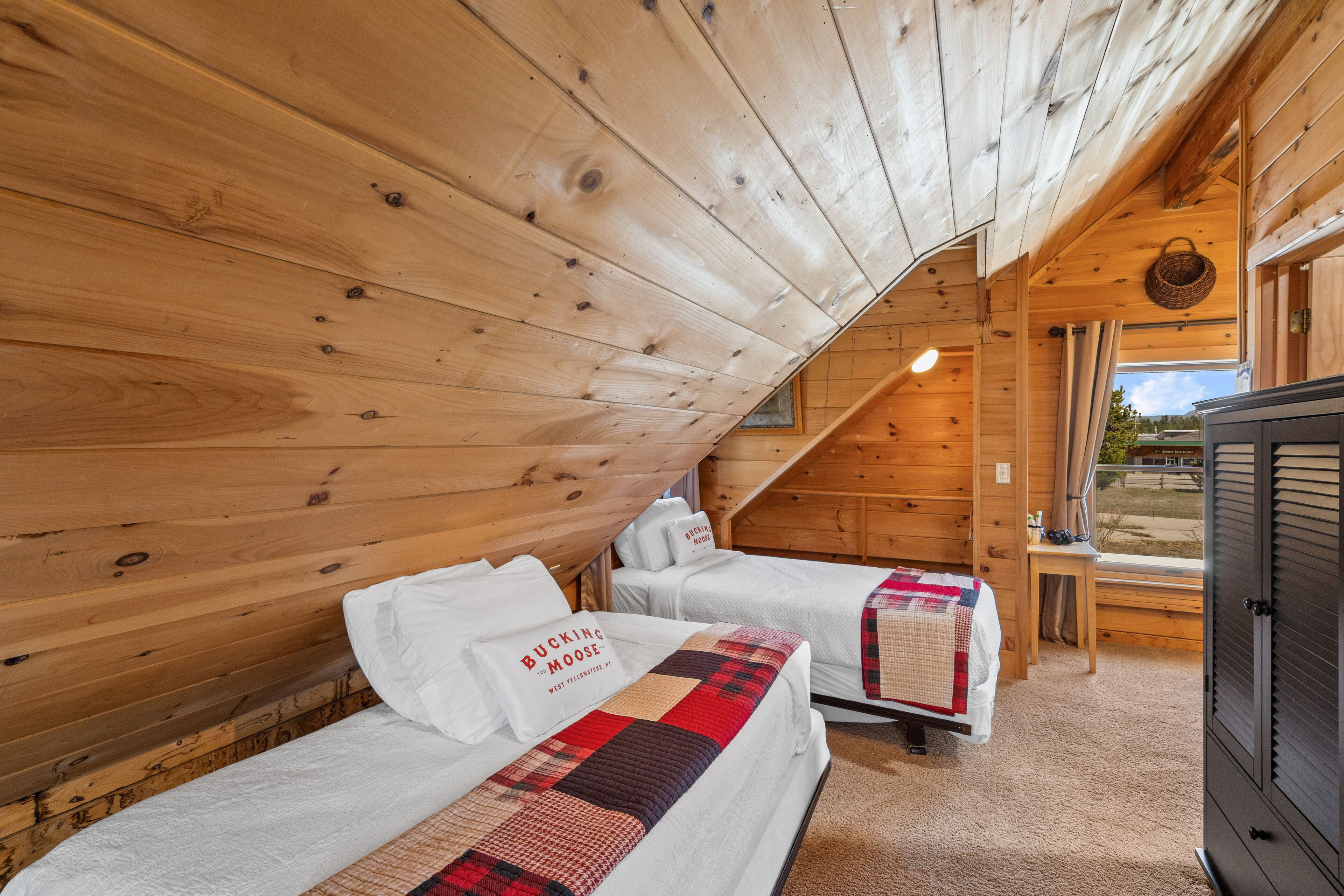 A cozy cabin with two beds, a wooden ceiling, and a window overlooking a scenic view.
