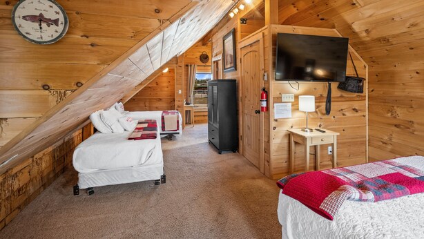 A cozy wooden cabin room with a bed, a desk, a television, and a clock on the wall.
