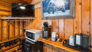 Interior de una cabaña de madera con televisor, cafetera, microondas y un cuadro con un oso.