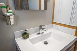 A bathroom with a white sink, chrome faucet, and a small green soap dispenser.