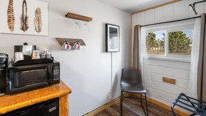 Une cuisine équipée d’un four à micro-ondes, d’une machine à café et d’un meuble en bois. On y trouve une chaise et un banc près d’une fenêtre donnant sur des arbres.
