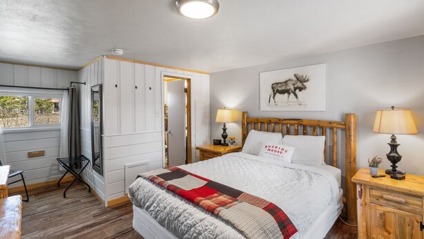 Une chambre à coucher avec un grand lit, une tête de lit en bois, une table de chevet avec une lampe, une fenêtre avec des rideaux et une porte donnant sur une autre pièce.