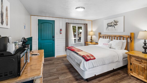 A bedroom with a bed, a desk with a computer, a teal door, and a window with curtains. - The Gopher Queen Room at The Bucking Moose, just 1 minute from Yellowstone in West Yellowstone. (West Yellowstone)