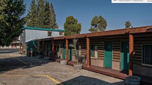 A row of log cabins with green doors and windows, a metal building with a green roof, and a gravel parking area.