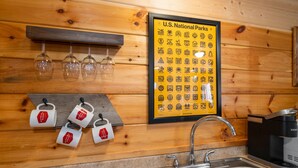 A kitchen with a sink, a coffee maker, and a framed poster of U.S. National Parks symbols.