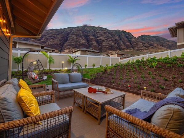 An outdoor patio with wicker furniture, a hanging chair, and a view of a mountainous landscape.