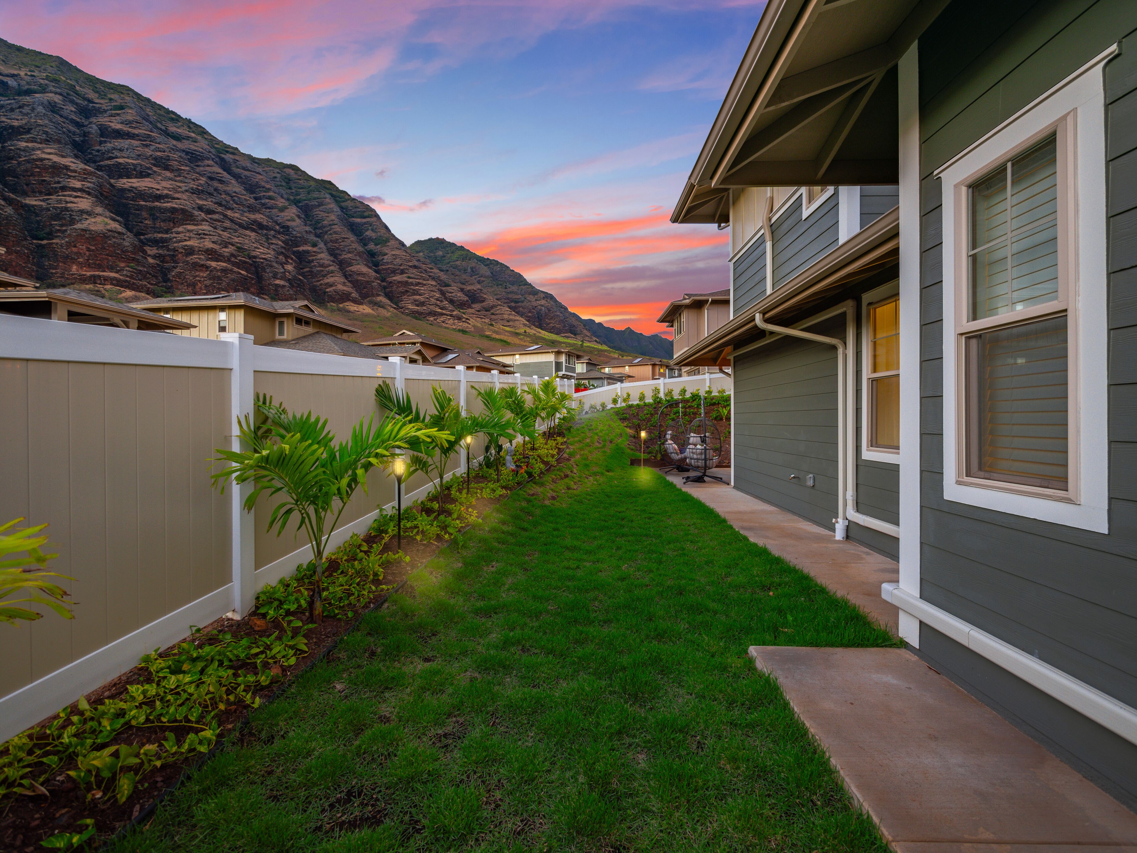 A residential area with a well-maintained lawn, a white fence, and houses with grey siding and white trim.