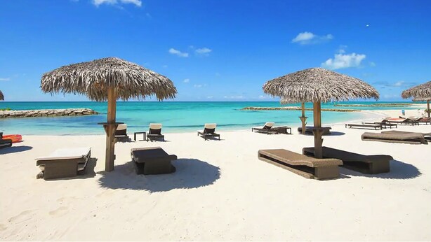 A beach with thatched umbrellas, lounge chairs, and a clear blue sky. - Modern Luxury Townhome in Nassau - steps to the beach! (Nassau)