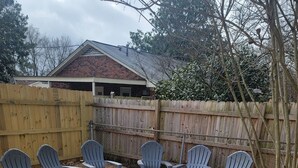 Un patio trasero con un pozo de fuego rodeado de sillas Adirondack, una valla de madera y una casa al fondo.