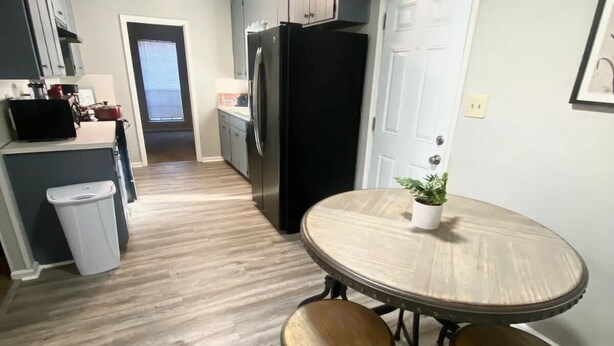 Una cocina compacta con un refrigerador negro, un basurero pequeño y una mesa de comedor con taburetes.