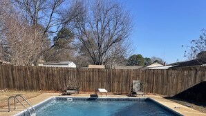 Una piscina rectangular con agua cristalina, rodeada por una valla de madera y algunas sillas al aire libre.