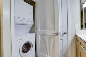 Laundry room with a front-loading washer and dryer, a countertop, and a window with blinds.