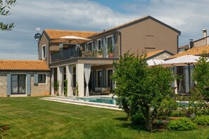 Una casa de dos pisos con piscina, balcón y jardín.