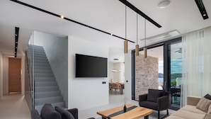 A modern living room with a staircase, a flat-screen TV, and a dining area. - Luxury Villa Siesta with Pool (Jezera)