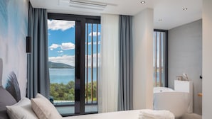 A modern hotel room with a large bed, a view of the sea, and a bathroom with a bathtub. - Luxury Villa Siesta with Pool (Jezera)