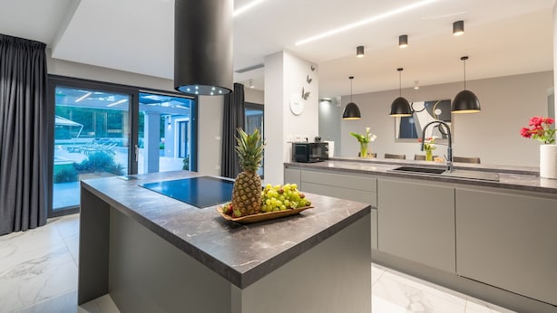 Una cocina moderna con una isla central, horno empotrado y un amplio ventanal con vistas a una zona de piscina.