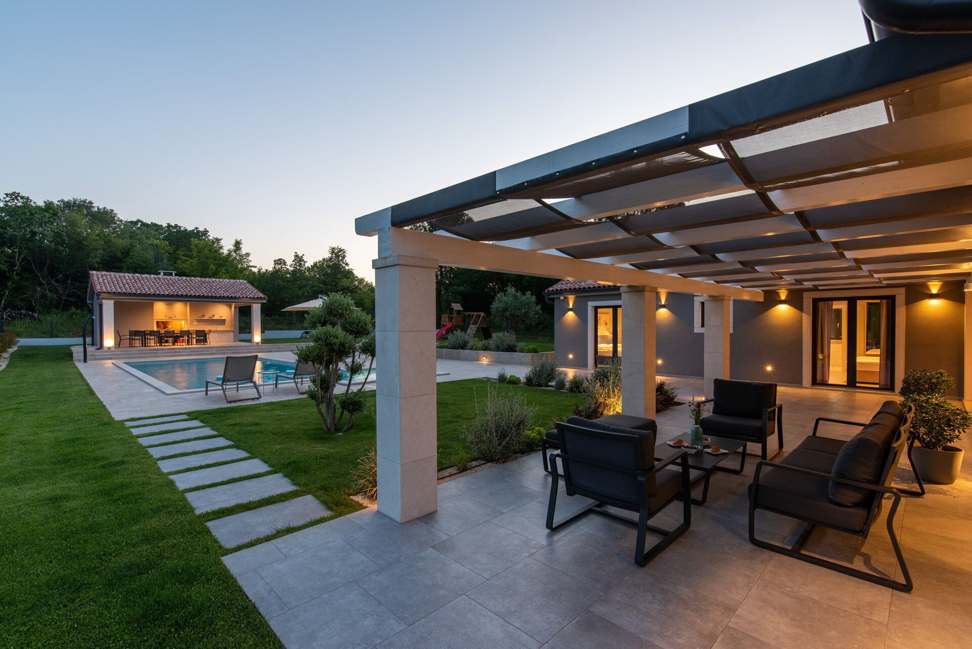 Een modern terras buiten met een zwembad, zithoek en een overdeeld gedeelte met sfeerverlichting.