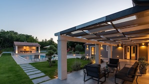 Un patio moderno al aire libre con piscina, zona de estar y una sección cubierta con iluminación ambiental.