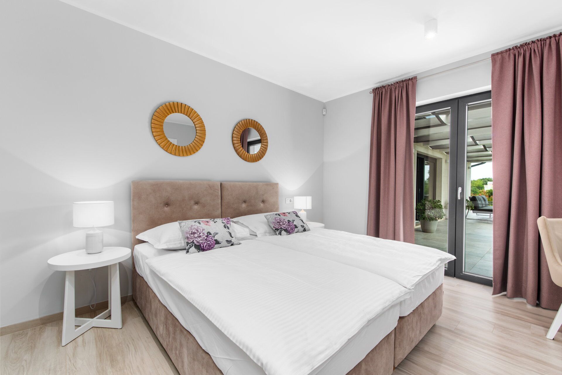 A modern hotel room with a large bed, two bedside tables, a mirror, and a view of the outdoors.