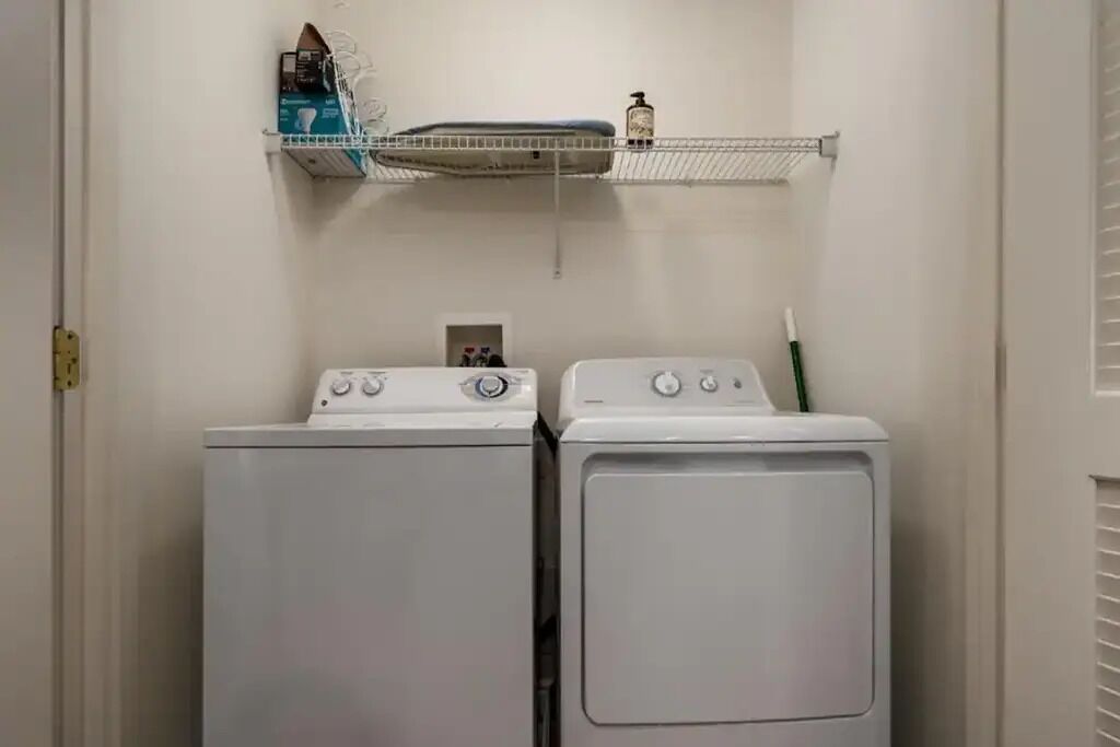 A laundry room with two white washing machines and a shelf above them holding a bottle and a box.