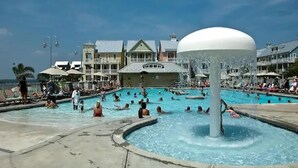 A swimming pool area with multiple pools, a water fountain, and a building with a green roof in the background. - ⭐️Gorgeous Sunset Island Private Beach In/Outdoor Pools⭐️ (Ocean City)