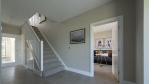 Un pasillo espacioso con una escalera empapelada, un cuadro en la pared y una zona de estar con sofá y mesa.