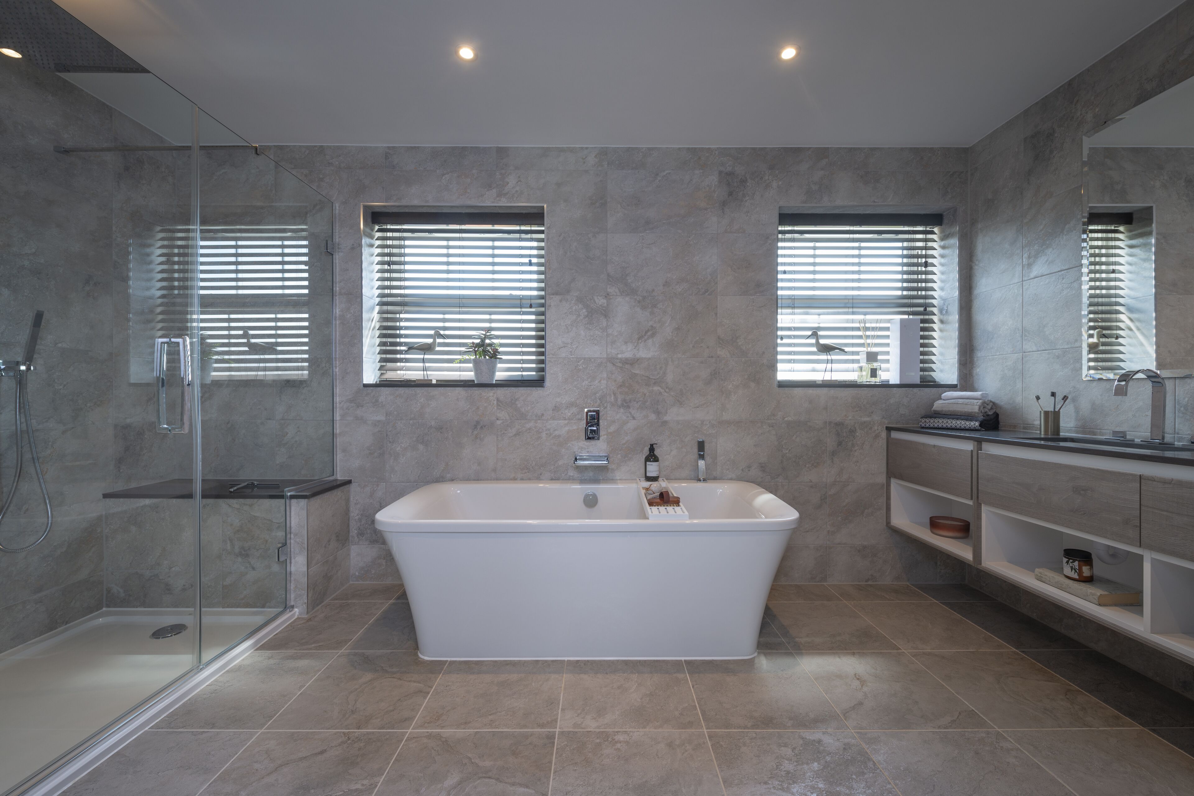 Een moderne badkamer met een vrijstaand bad, een douche met glazen wanden en een badkamermeubel met planken.