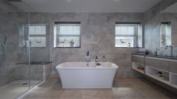 Een moderne badkamer met een vrijstaand bad, een douche met glazen wanden en een badkamermeubel met planken.
