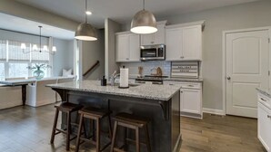 Une cuisine moderne dotée d’un grand îlot central, de luminaires suspendus, de meubles blancs et d’un four à micro-ondes.