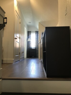 Enter a cozy space with a kitchen area visible through the doorway, featuring a refrigerator and a window with patterned curtains.