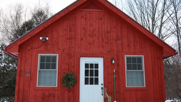 A red wooden house with a white door, two windows, and a small wreath on the door. - Guest House 10 Min to Smugglers! (Cambridge)