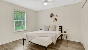 A bedroom with a bed, a ceiling fan, a window with blinds, and a small bedside table with a lamp. - Entire Home: Coastal 3BR Escape with Garage & Pets (St. Augustine)