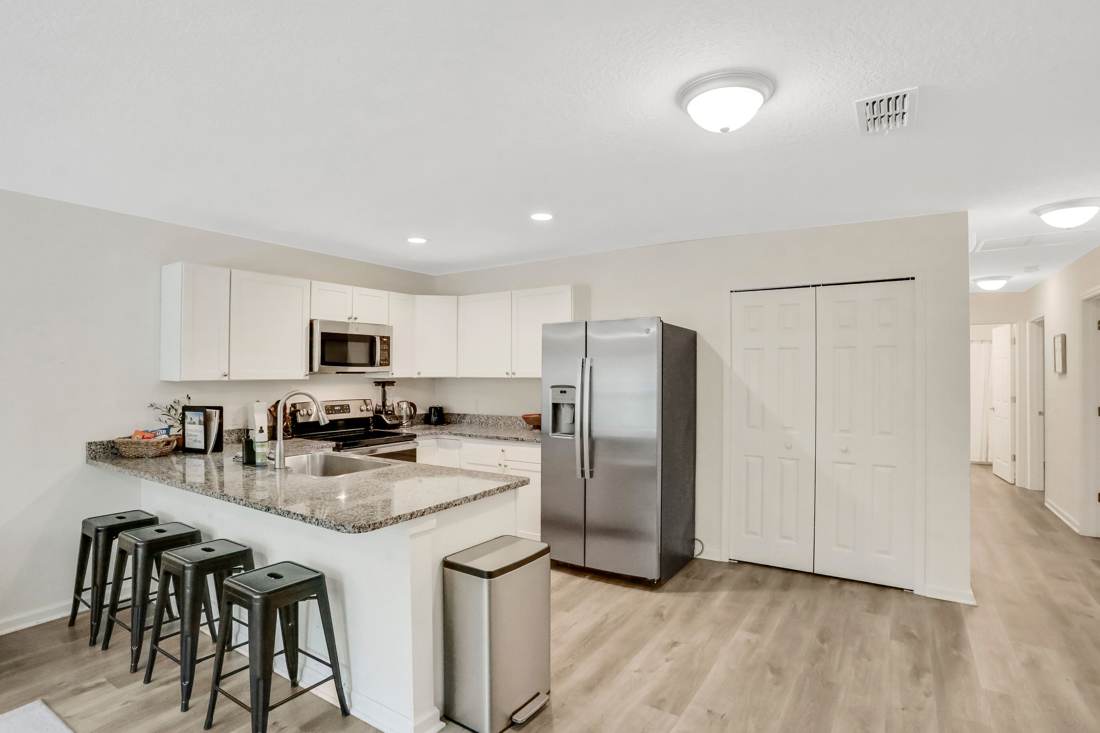 A modern kitchen with white cabinets, a stainless steel refrigerator, a granite countertop, and a built-in microwave.