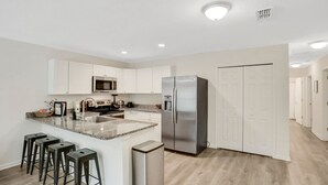 A modern kitchen with white cabinets, a stainless steel refrigerator, a granite countertop, and a built-in microwave. - Entire Home: Coastal 3BR Escape with Garage & Pets (St. Augustine)