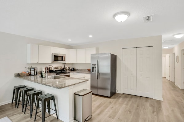 A modern kitchen with white cabinets, a stainless steel refrigerator, a granite countertop, and a built-in microwave.