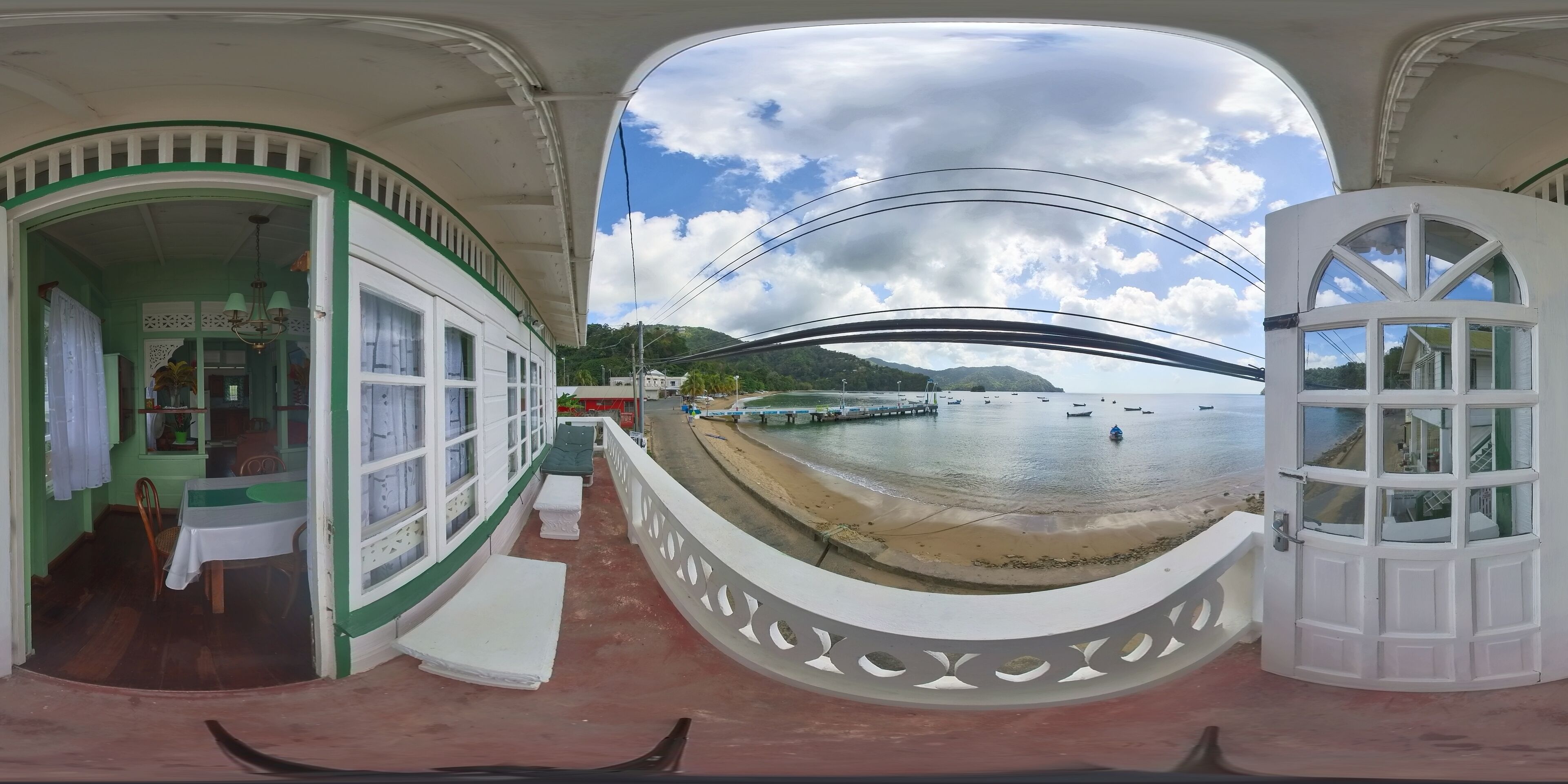 Una habitación con vista a una playa y barcos, un comedor con mesa y sillas, y una baranda decorativa.