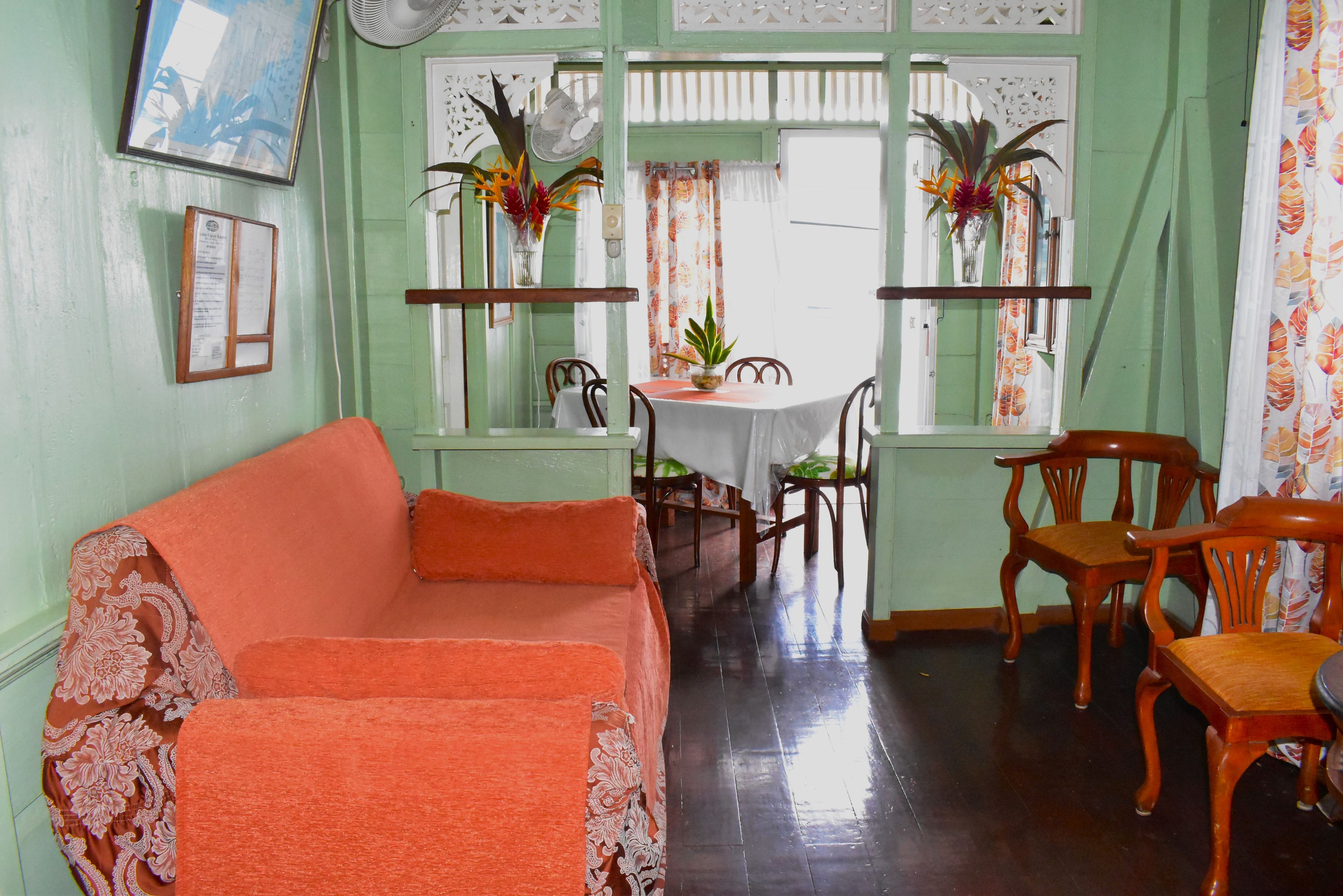 A room with a green wall, a wooden dining table with chairs, a sofa, and a fan.