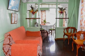 A room with a green wall, a wooden dining table with chairs, a sofa, and a fan. - CHOLSON CHALETS LIMITED (Charlotteville)