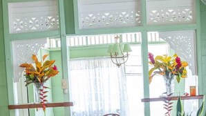 A room with a wooden floor, a green wall, a wooden chair, a table with a green plant, and a bed with an orange cover. - CHOLSON CHALETS LIMITED (Charlotteville)
