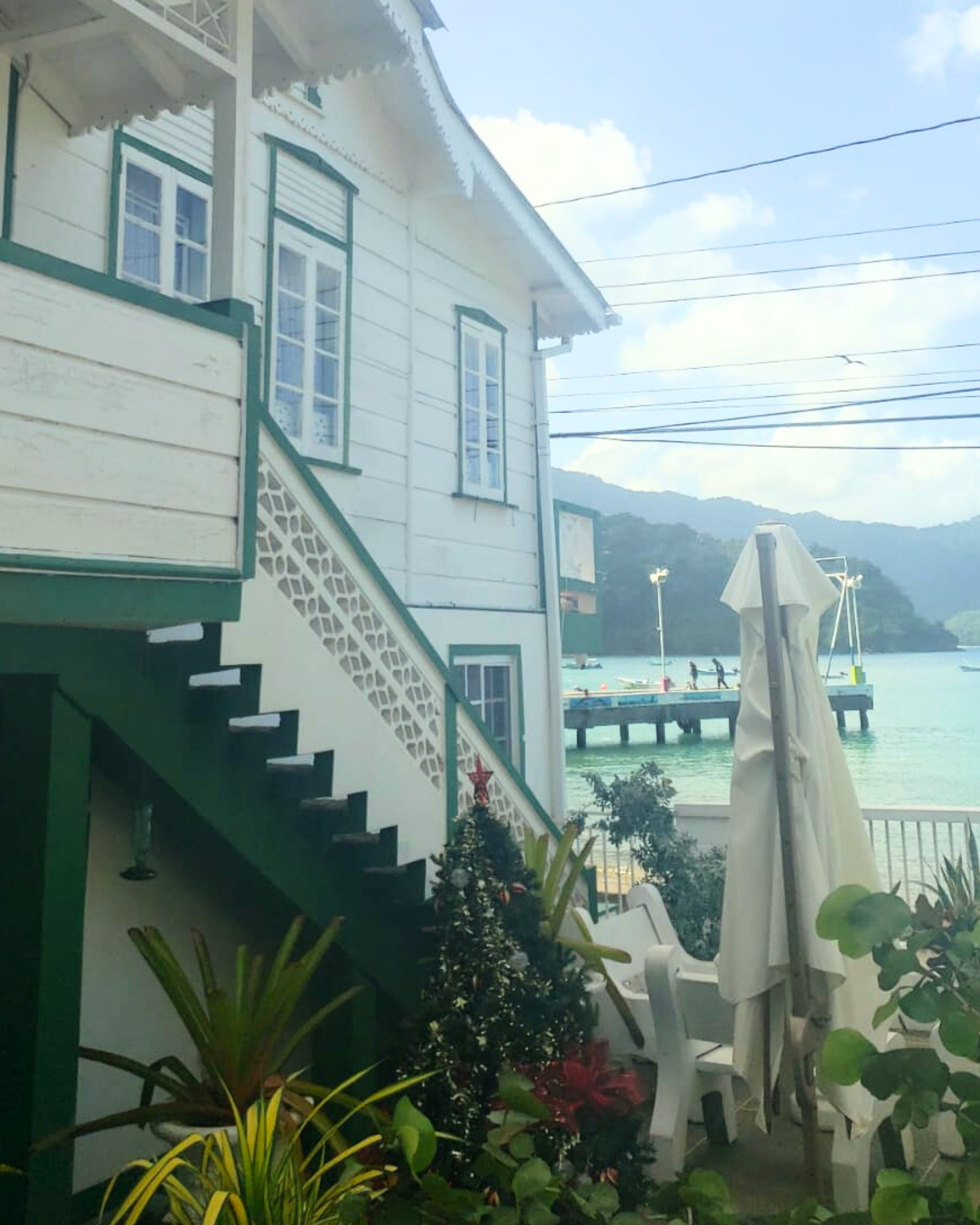 A white building with green trim, a staircase leading to a balcony, and a view of a pier and water.