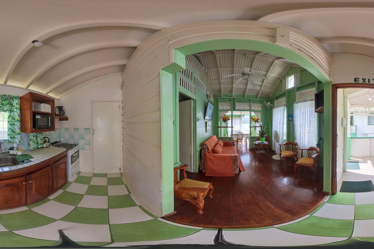 A kitchen with a checkered floor, wooden cabinets, a refrigerator, and a dining area with chairs and a sofa.
