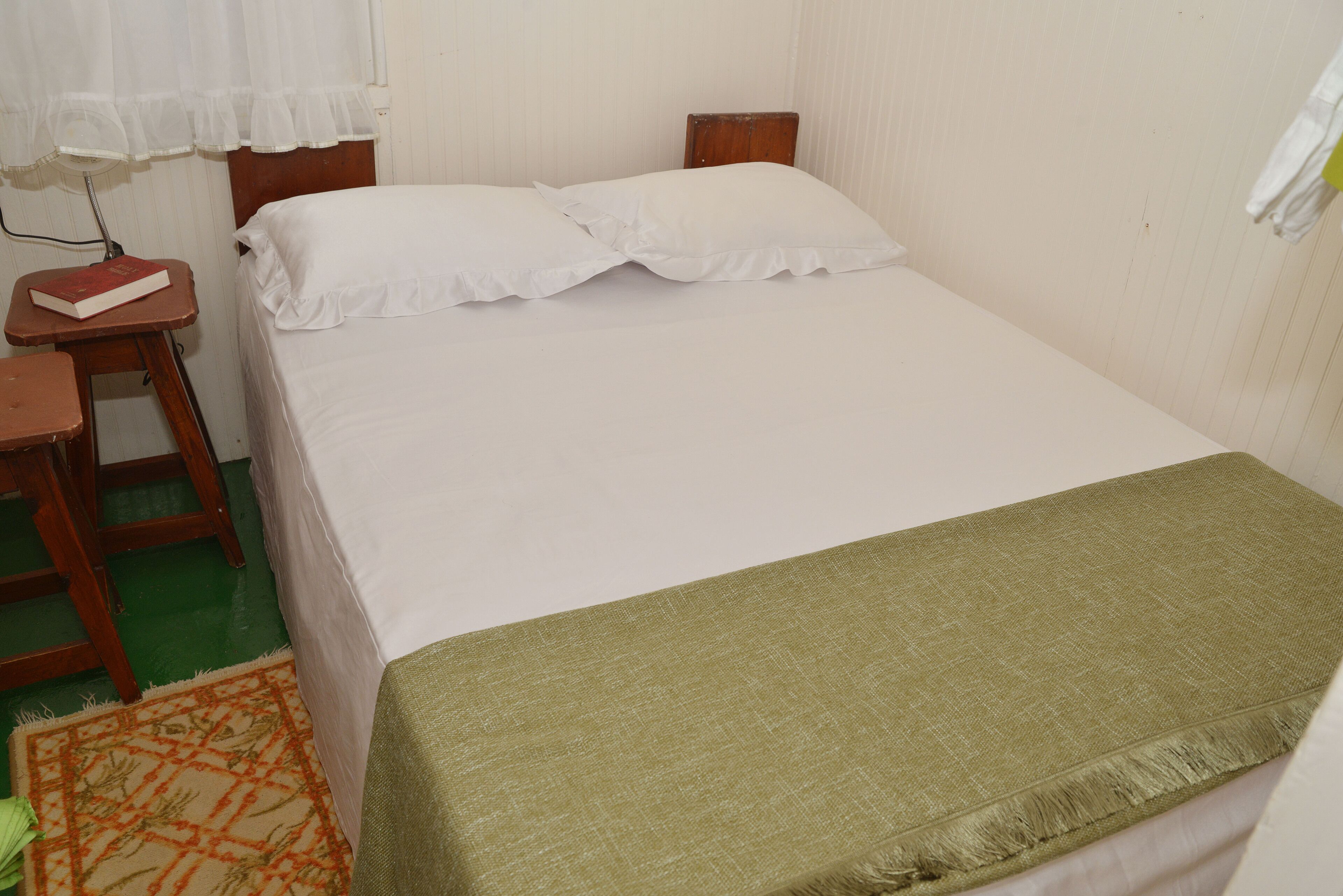 A simple room with a bed, a nightstand, a chair, and a small table.