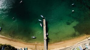 An aerial view of a coastal area with a pier extending into the sea, surrounded by clear waters and several boats. There are buildings and parked cars along the shore. - CHOLSON CHALETS LIMITED (Charlotteville)