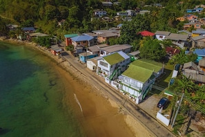 An aerial view of a coastal residential area with houses along the beach, clear water, and dense greenery. - CHOLSON CHALETS LIMITED (Charlotteville)