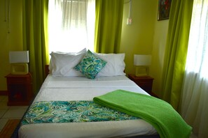 A bed with a patterned bedspread and pillows, two bedside lamps, and a window with curtains. - CHOLSON CHALETS LIMITED (Charlotteville)
